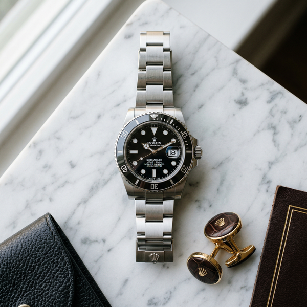 Rolex Submariner on marble surrounded by luxury accessories