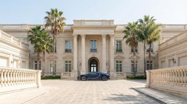 Daytime facade of a luxury mansion with a stunning Bugatti parked in front.