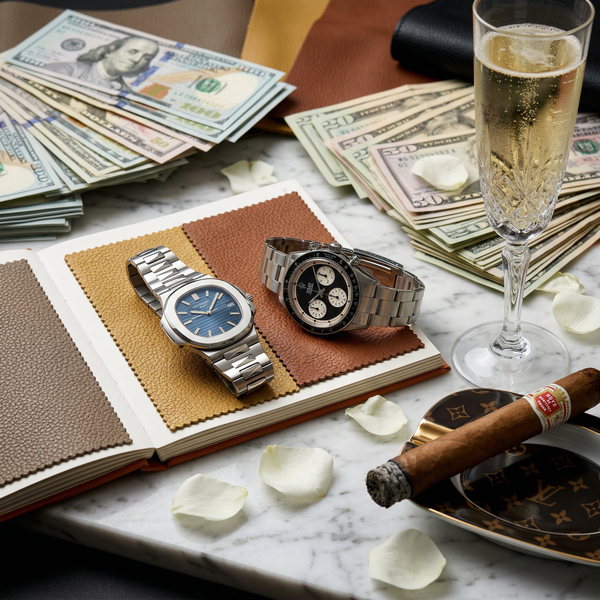 Patek and Rolex on marble beside stacks of cash and Cristal
